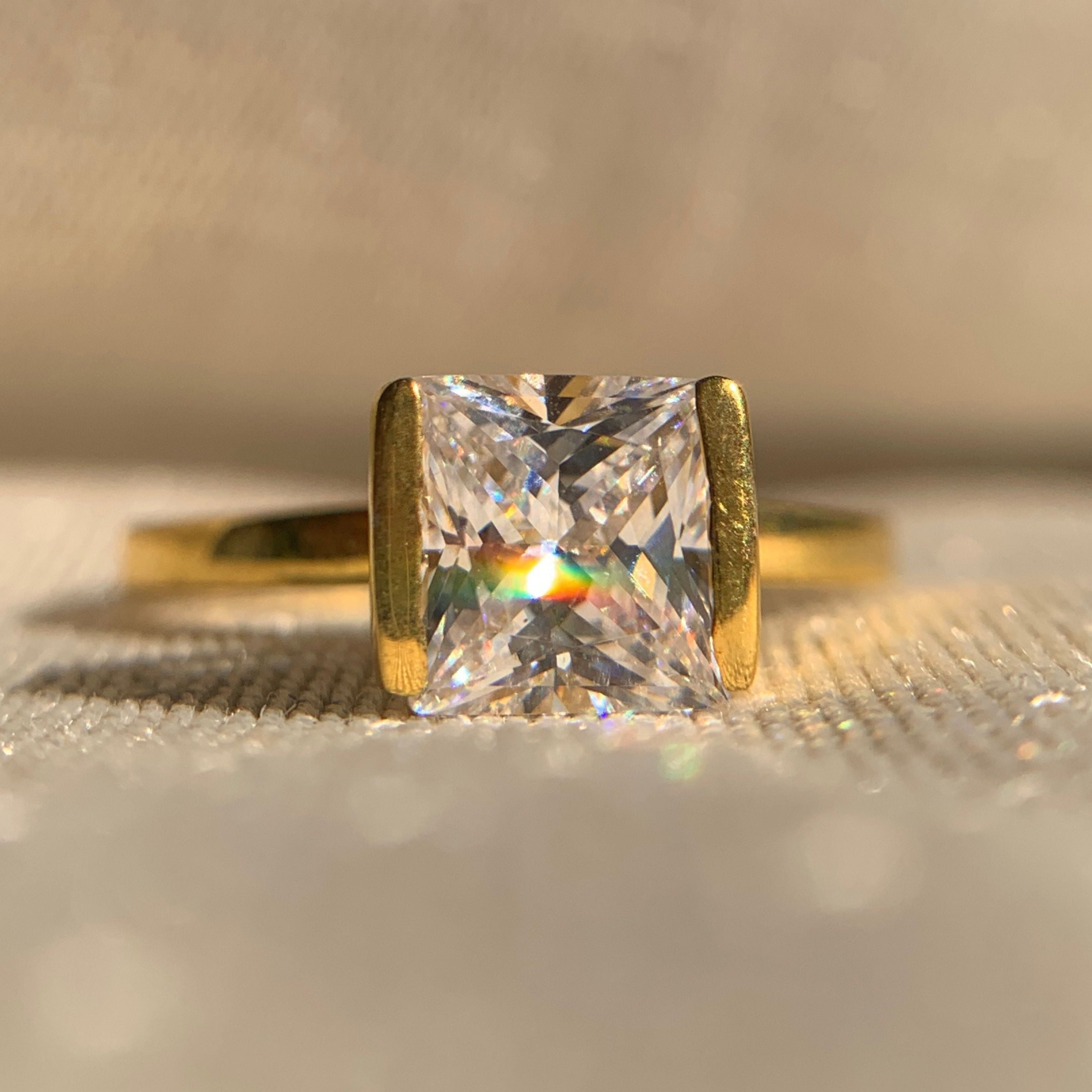 Engagement Ring Princess Half Bezel Setting on a textured beige surface